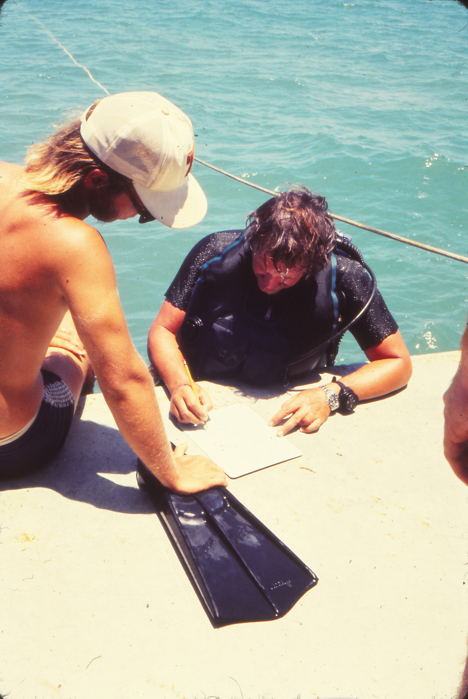 In a 1970s photo, two men in snorkeling gear chat near the water