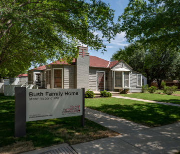 A gray single-story midcentury home with a Texas Historical Commission sign in front identifying it as the Bush Childhood Home