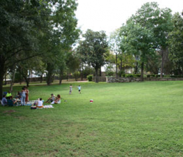 A group of people of varying ages seated on an expanse of green rolling lawns with a historic house in the background.