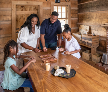 Photo of family (mom, dad, and two young girls) gathered around a table playing backgammon together