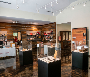 Inside the Levi Jordan Plantation Visitor Center, with artifacts inside glass cases throughout the room, books appear on shelves with wooden paneling on the walls 