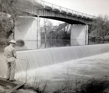 Fisherman by dam below highway bridge