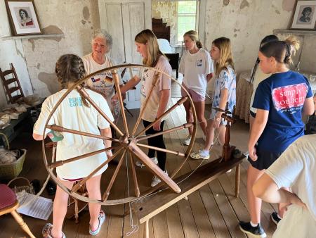 A living historian demonstrating how to use a spinning wheel to a group of students.