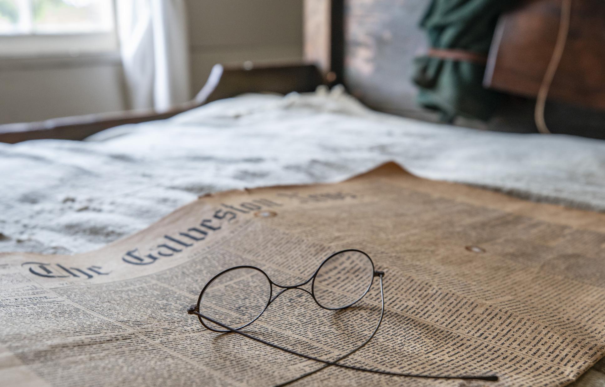 Newspaper laying on a bed with glasses on top
